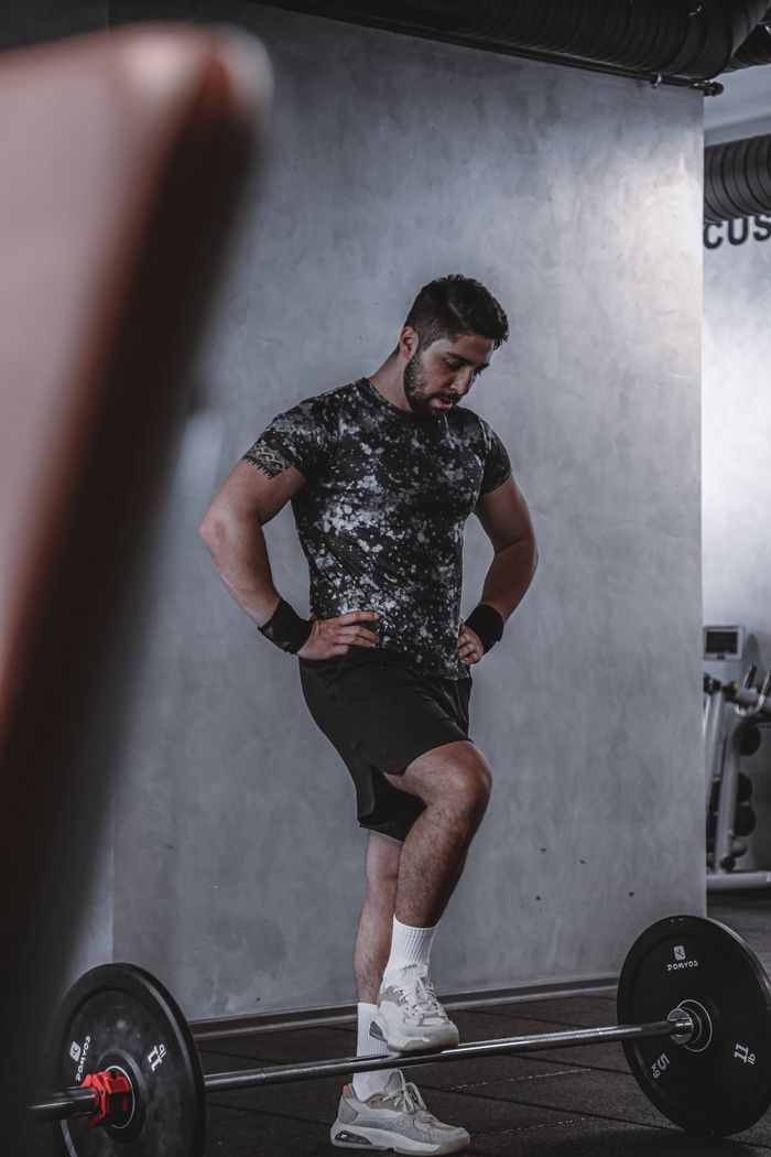 services-04 Adult male athlete resting in a gym after lifting weights with a barbell. Indoor fitness lifestyle scene.