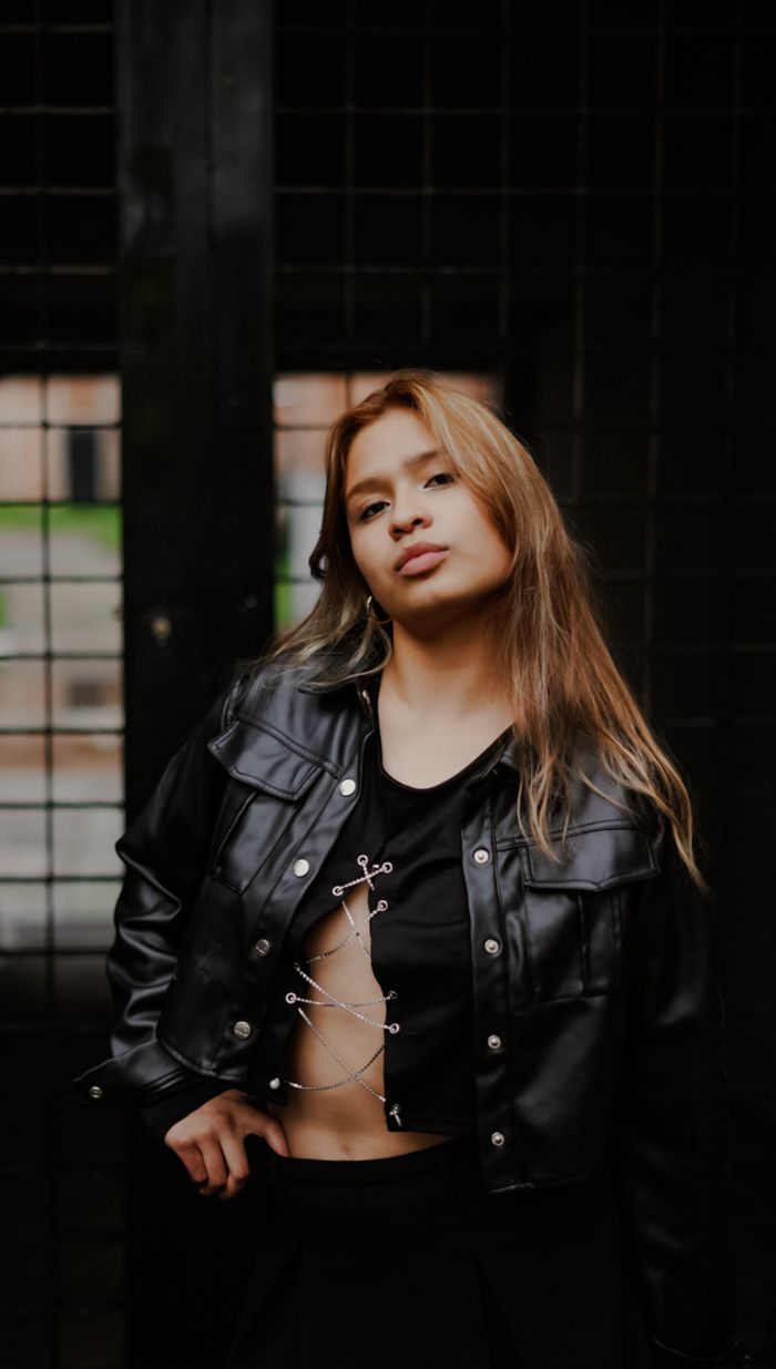 Stylish young woman in black outfit posing confidently outdoors, embodying modern urban fashion.
